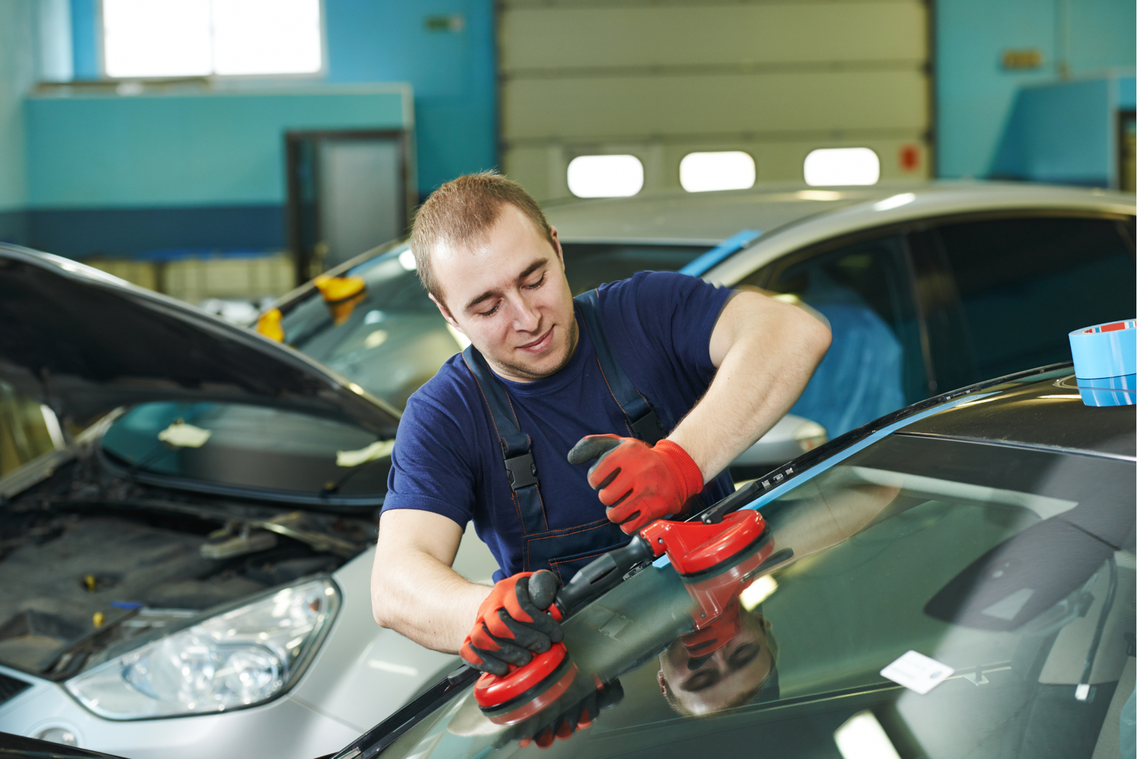 Un apprentis technicien vitrage automobile utilisant les ventouses pour remplacer un pare-brise