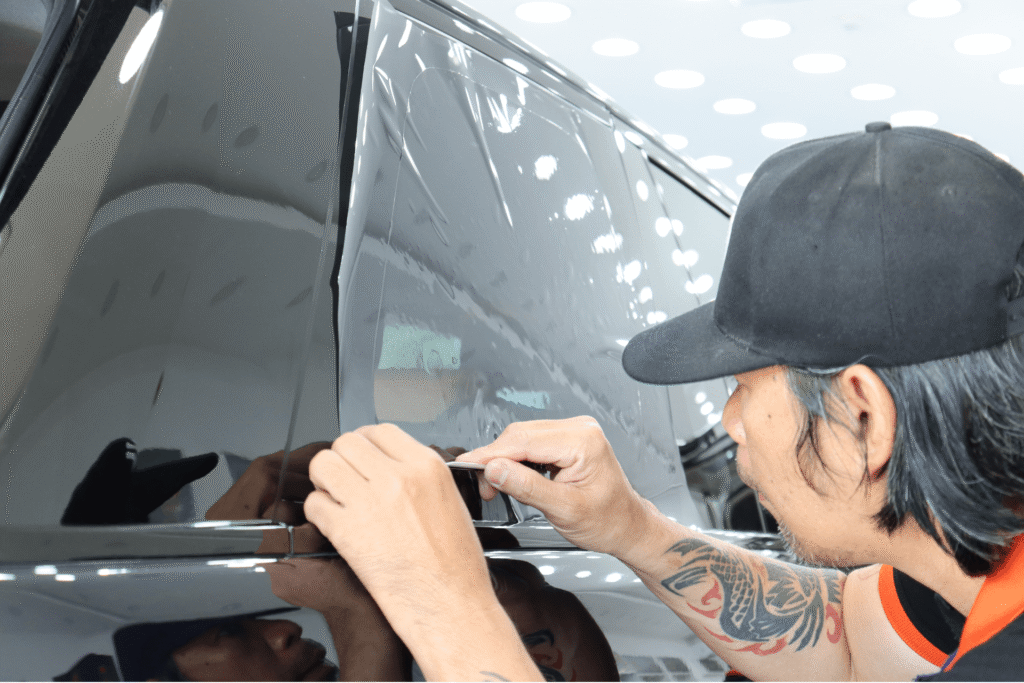 Un élève en démonstration de pose d'un film solaire sur une voiture durant une formation vitre teintée automobile